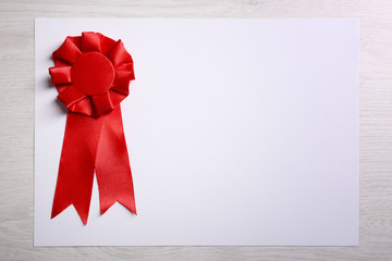 Award ribbon on white paper sheet, on wooden background