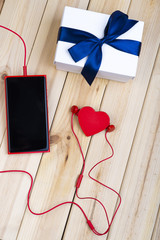 Red Smart Phone With Blank Screen, Red Earphones, White Gift Box With Blue Ribbon And Little Red Heart On Pine Boards. Love Concept.