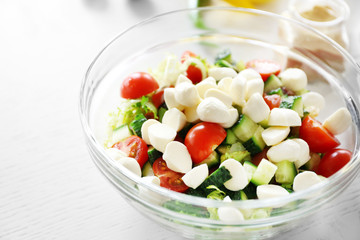 Tasty salad in glass dish on color wooden table background
