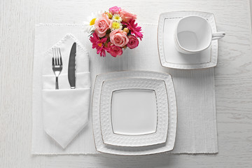 Table setting with dishes, cutlery and flowers on white background