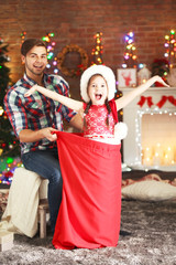 Obraz premium Funny little sister in Santa sack surprising her older brother on Christmas background