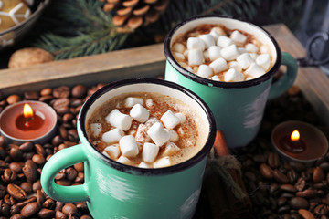 Two mugs of hot cacao with marshmallow on coffee beans