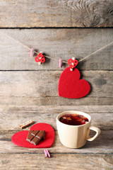 Cup of tea with piece of chocolate on red heart and clothespins on wooden background closeup