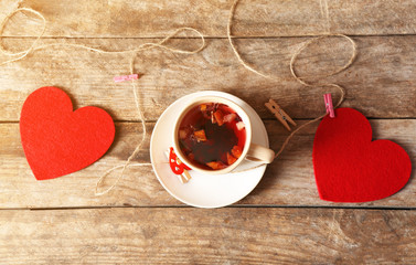 Cup of tea with two red hearts and rope with clothespins on wooden background closeup