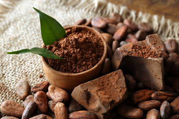 Bowl with aromatic cocoa powder and green leaf on a sacking, close up