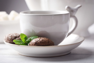 Cup of coffee with chocolate chip cookies and mint on light background