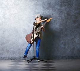 Fototapeta premium Little boy playing guitar and singing with microphone on a grey wall background