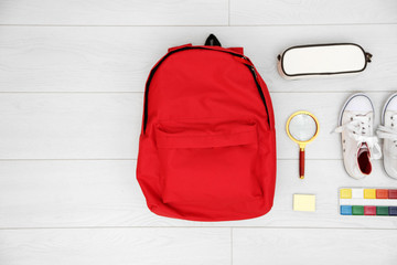 School set with backpack, shoes and supplies on light wooden background