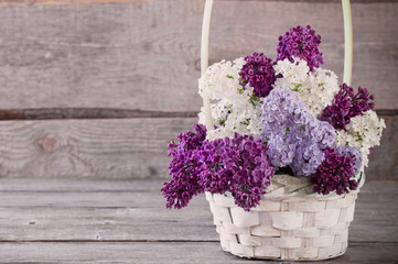 basket with a branch of lilac flower on a wooden background