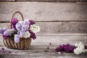 basket with a branch of lilac flower on a wooden background