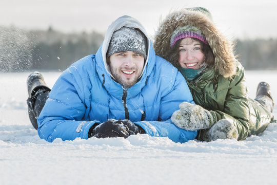 Young couple having fun outdoors lying on snowy ground covering in winter snowing day