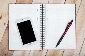White Smart Phone With Blank Black Screen, Notebook And Pencil On Wooden Desk.