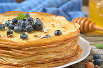 Stack of delicious pancakes with blueberries, honey and hazelnuts on plate and napkin on wooden background