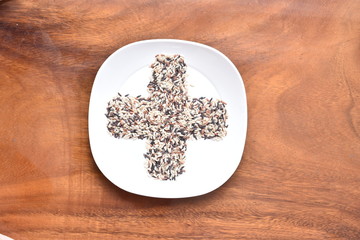 Plus shape of rice in white dish on wooden background.