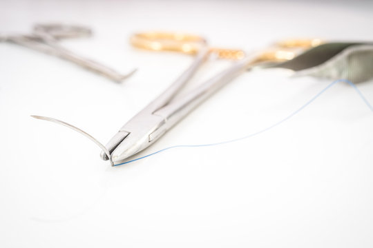 Close up of needle holder with suture and needle, forceps and su