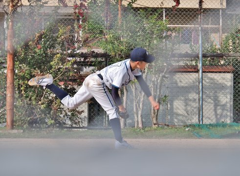 Young Japanese baseball player no.17 pitching by left hand. This photo was taken through a wire mesh fence.