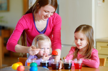 Young mother and her two daughters painting Easter eggs