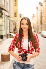 Pretty young girl holding camera and standing on the street