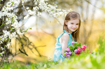Adorable little girl holding tulips for her mother in cherry garden