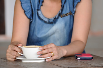 Asian woman relaxing with smartphone and coffee.