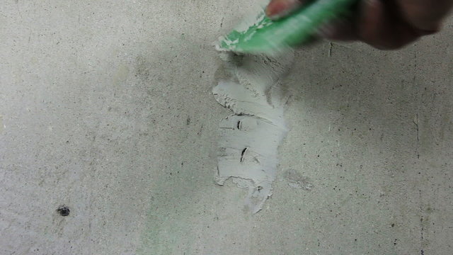 DIY,  close up of man's hand applying plaster filler to holes in interior wall. The technique and results are clearly those of someone who is not a trade professional.