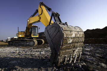 Yellow excavator in construction site with rocky ground and blue