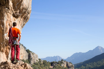 Fototapeta premium Young man climbing on a limestone wall with wide valley on the background
