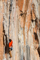 Fototapeta premium Young man climbing on a limestone wall with wide valley on the background