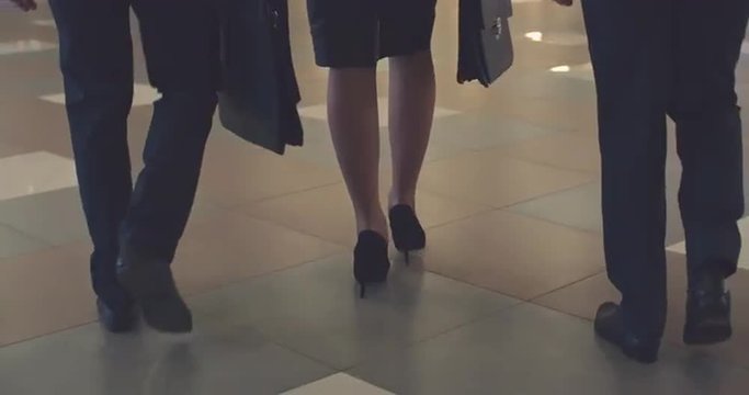 Rear view of legs of businesswoman and her two male colleagues walking on the floor of their office