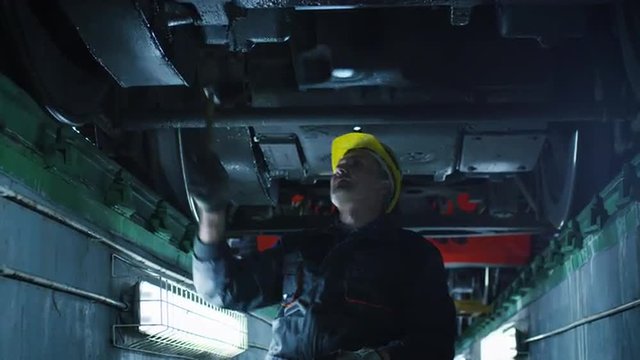 Technician in Hard Hat with Hammer in Hand Inspecting Train. Shot on RED Cinema Camera.
