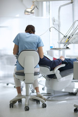 Fototapeta premium Rear view of a female doctor treating patient's teeth in a dental office