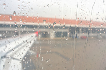 Drops of rain on glass window of airplane at airport background