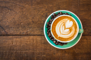 Latte hot coffee in green cup with latte art and roasted coffee beans. Wooden table background. Top view.