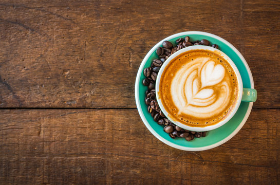 Latte hot coffee in green cup with latte art and roasted coffee beans. Wooden table background. Top view.