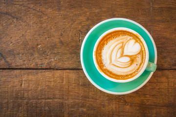 Latte hot coffee in green cup with latte art and saucer. Wooden table background. In coffee shop.