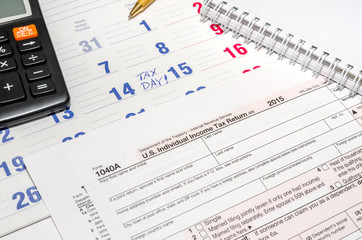 tax form with calculator, pen, notepad above paper calendar