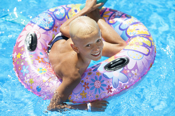 Młody chłopiec na wakacjach pływa w kole w basenie.