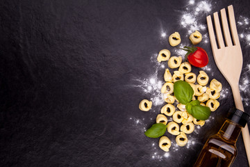 Fototapeta na wymiar Tortellini and flour on a black stone plate.