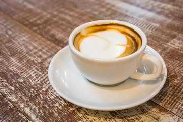 A cup of latte hot coffee with saucer. Wooden table background. In coffee shop.