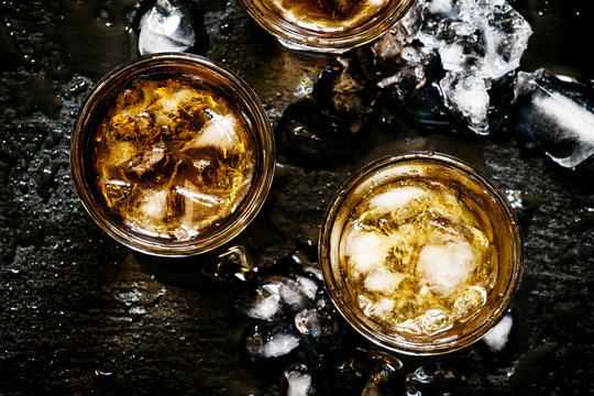 Cold whiskey in a glass with crushed ice on a black stone wet ba