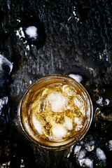 Cold whiskey in a glass with crushed ice on a black stone wet ba