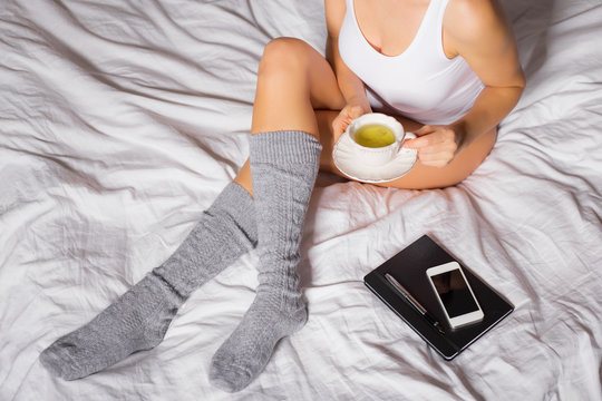 Woman with cup of tea and grey socks sitting in bed 
