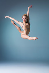 Fototapeta na wymiar Young beautiful modern style dancer jumping on a studio background