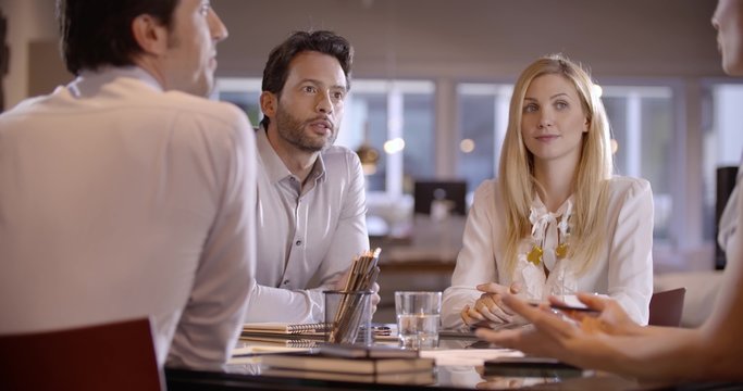 Four young collegues wearing formal dress have a business meeting talking each other about projects in office in slow motion (in realtime at 60 fps)