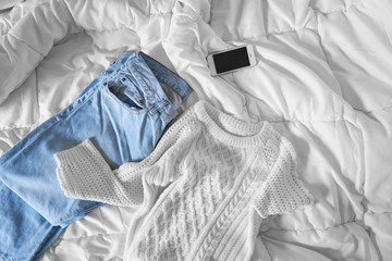 Female outfit and smartphone laid out on bed, morning light