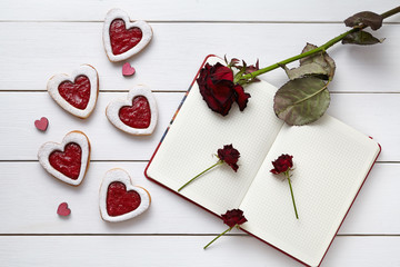 Heart shaped cookies with empty notebook and roses on white wooden background for Valentines day.