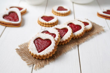Heart shaped cookies with jam, delicious homemade holiday surprise sweet on white wooden background for Valentines day celebration.