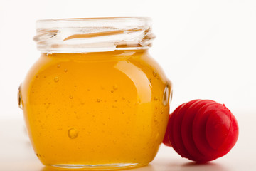 Glass jar filled with sweet sticky golden honey and red stick.