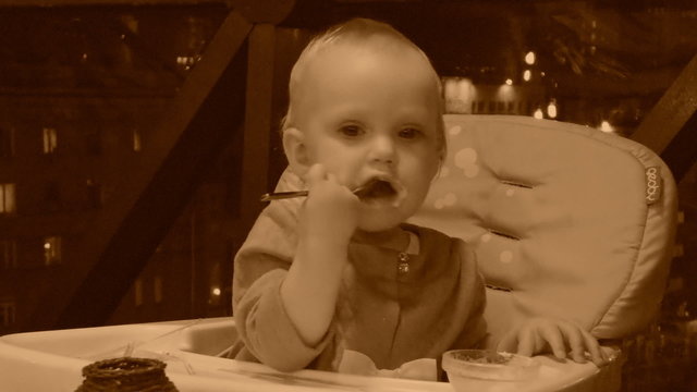 Little baby girl eats her dessert, old style sepia view with grain