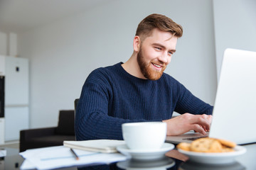 Fototapeta na wymiar Smiling man using laptop computer at home